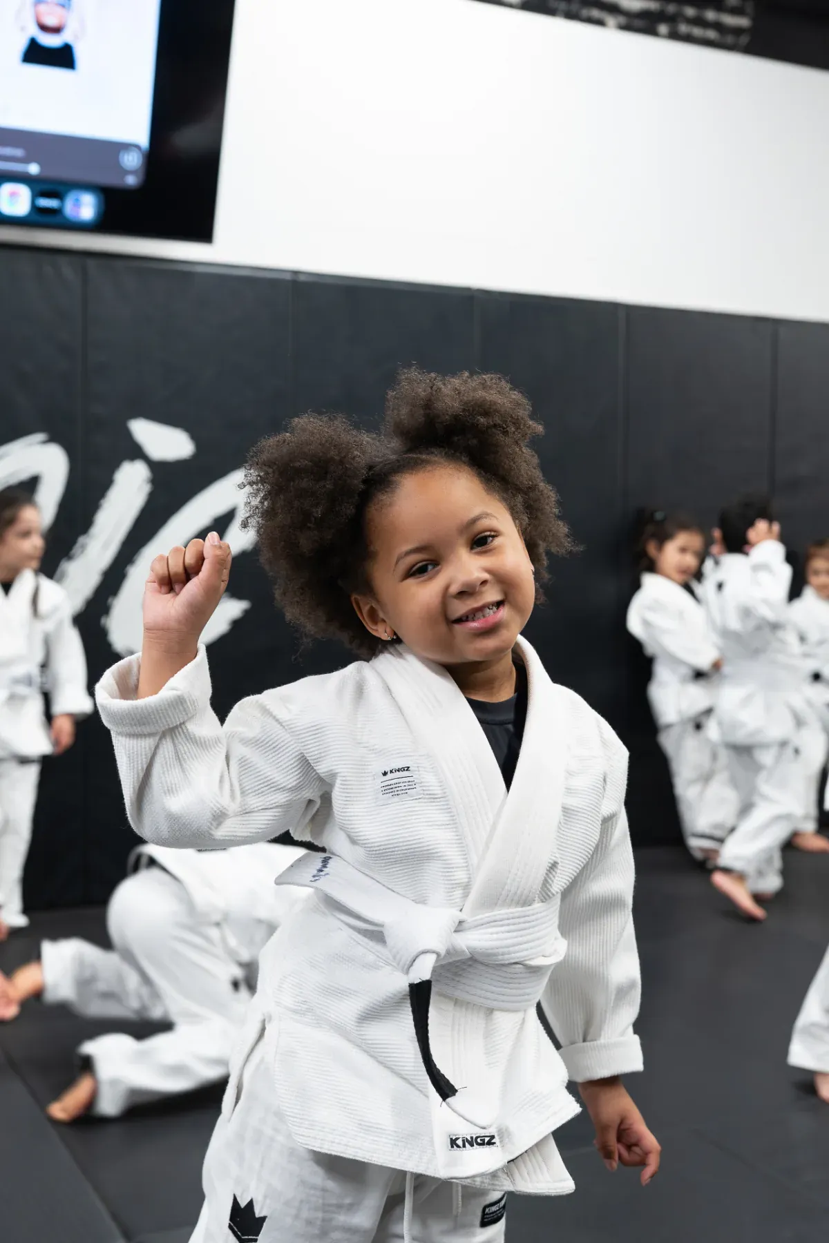Young Logic Jiu Jitsu student smiling confidently in her white Kingz gi during kids class