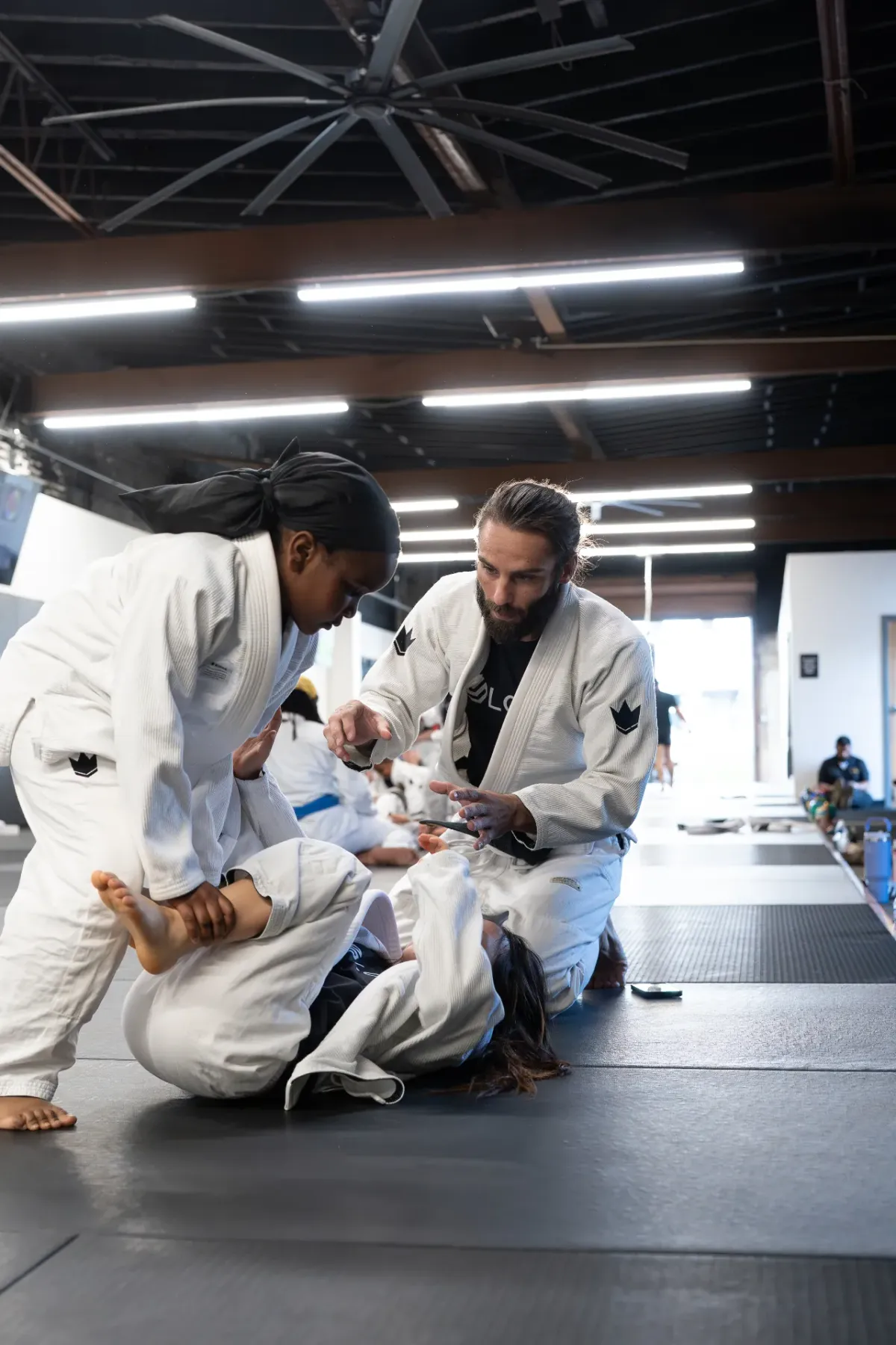 Coach Matt teaching a young girl a controlled Jiu Jitsu technique on the mat